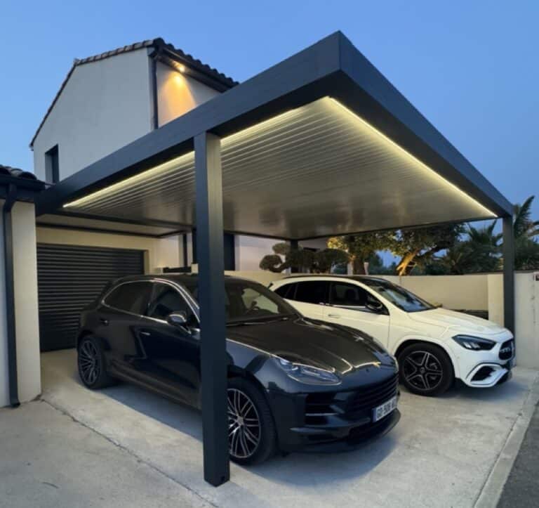Carport aluminium de nuit. Il est éclairé avec des néons, il y a deux belles berlines en dessous.